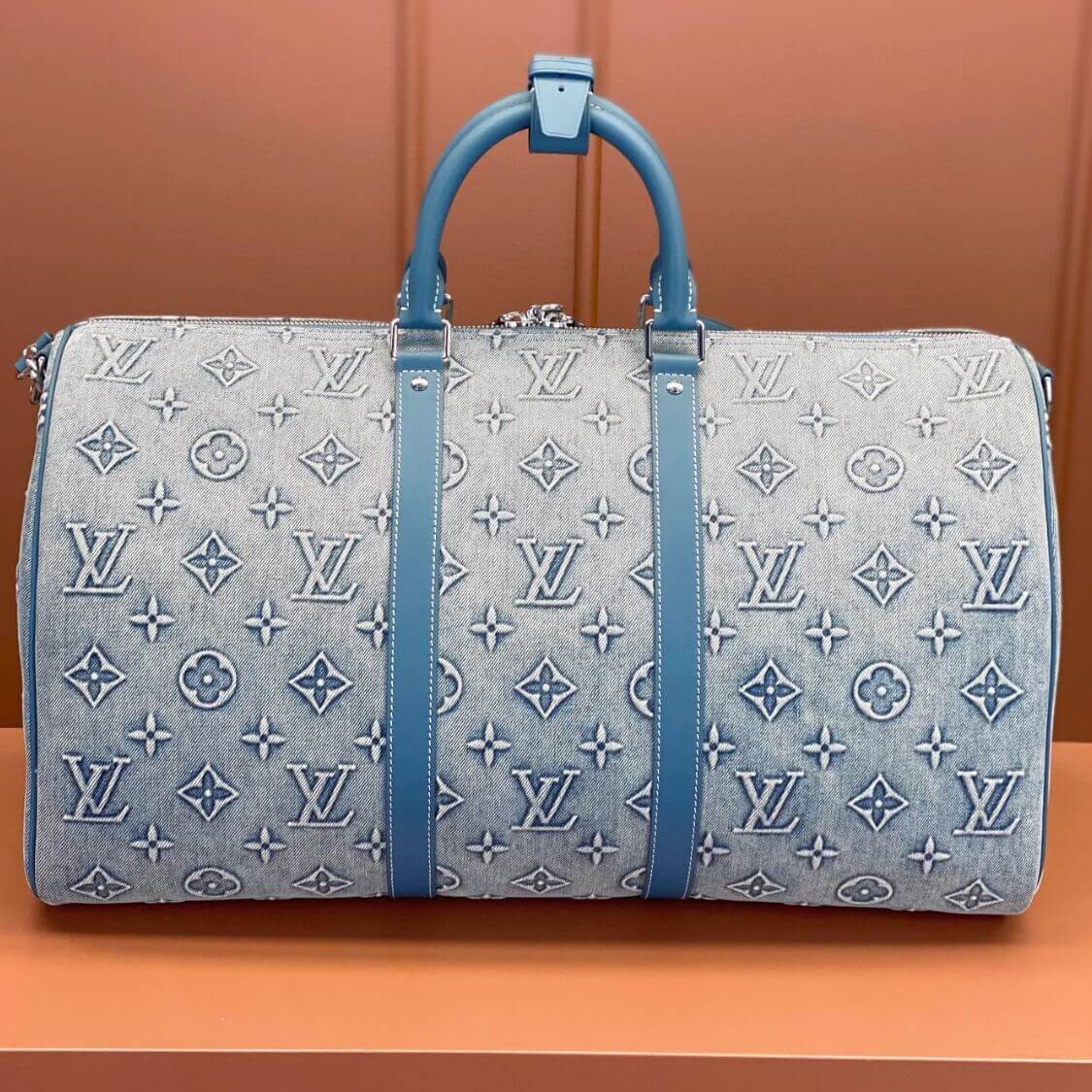 Louis Vuitton denim weekend bag with monogram print, blue leather handles, and vertical leather strap accents.