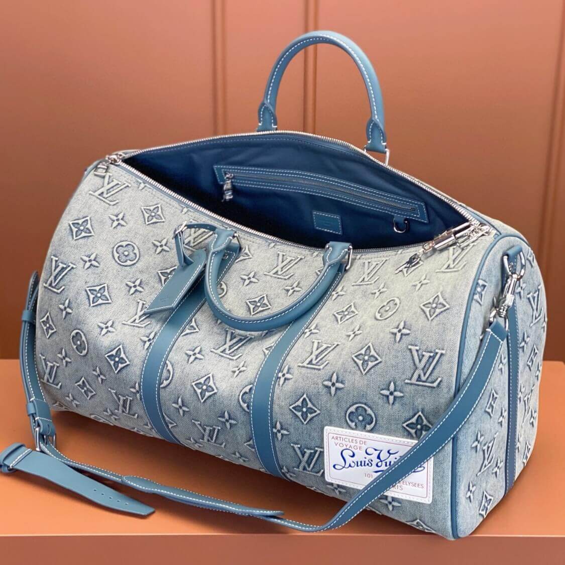 Louis Vuitton denim weekend bag with monogram pattern, blue leather trim, open top showing zippered interior pocket.