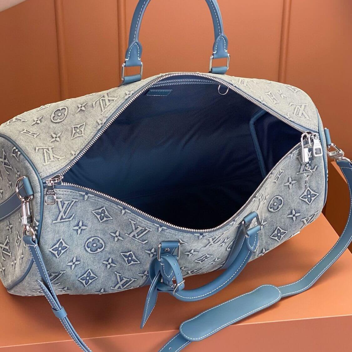Open Louis Vuitton denim weekend bag with monogram pattern, blue leather straps, and spacious dark interior.